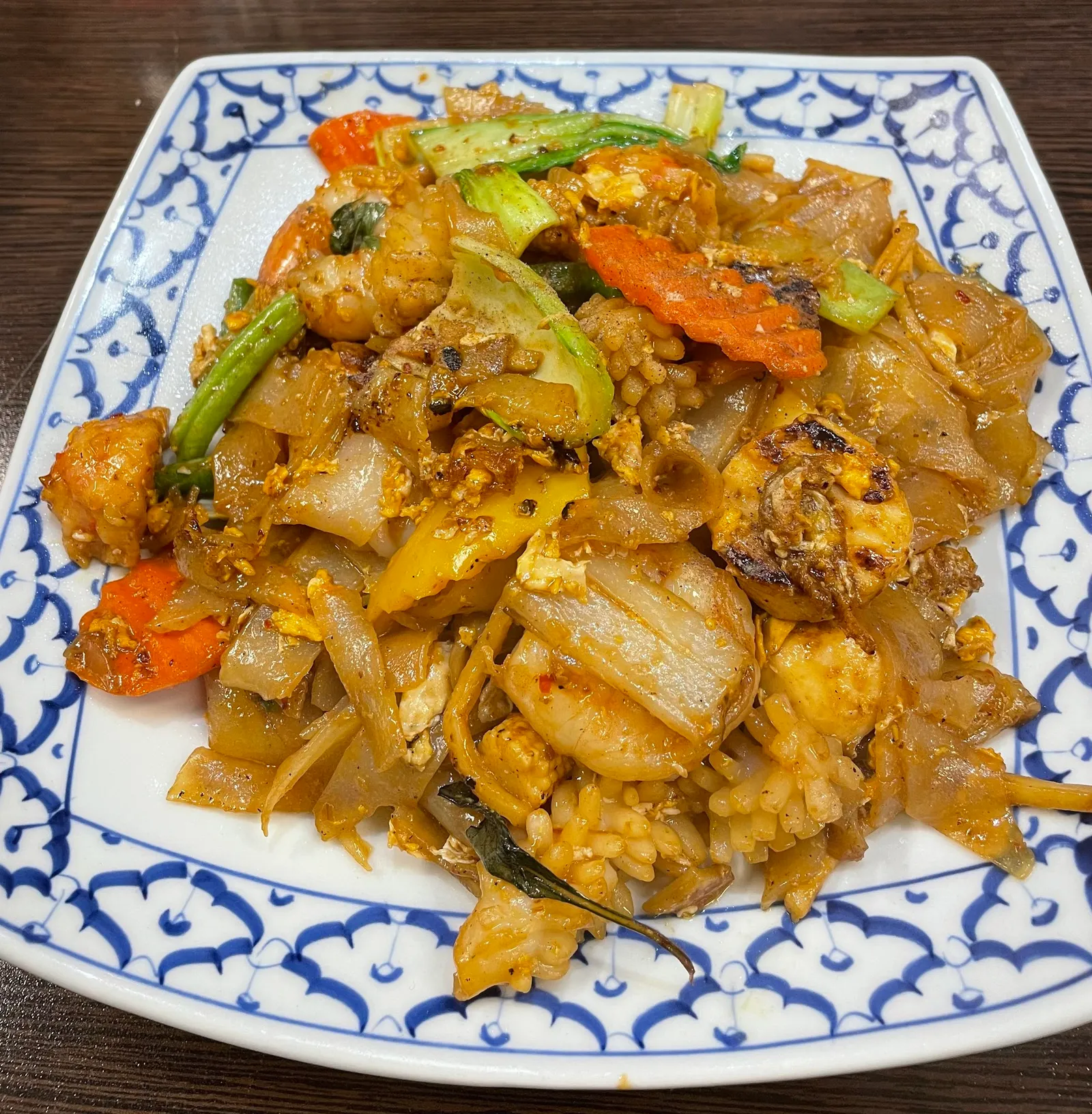Pad kee mao drunken noodles with prawns and vegetables on blue-white Thai plate