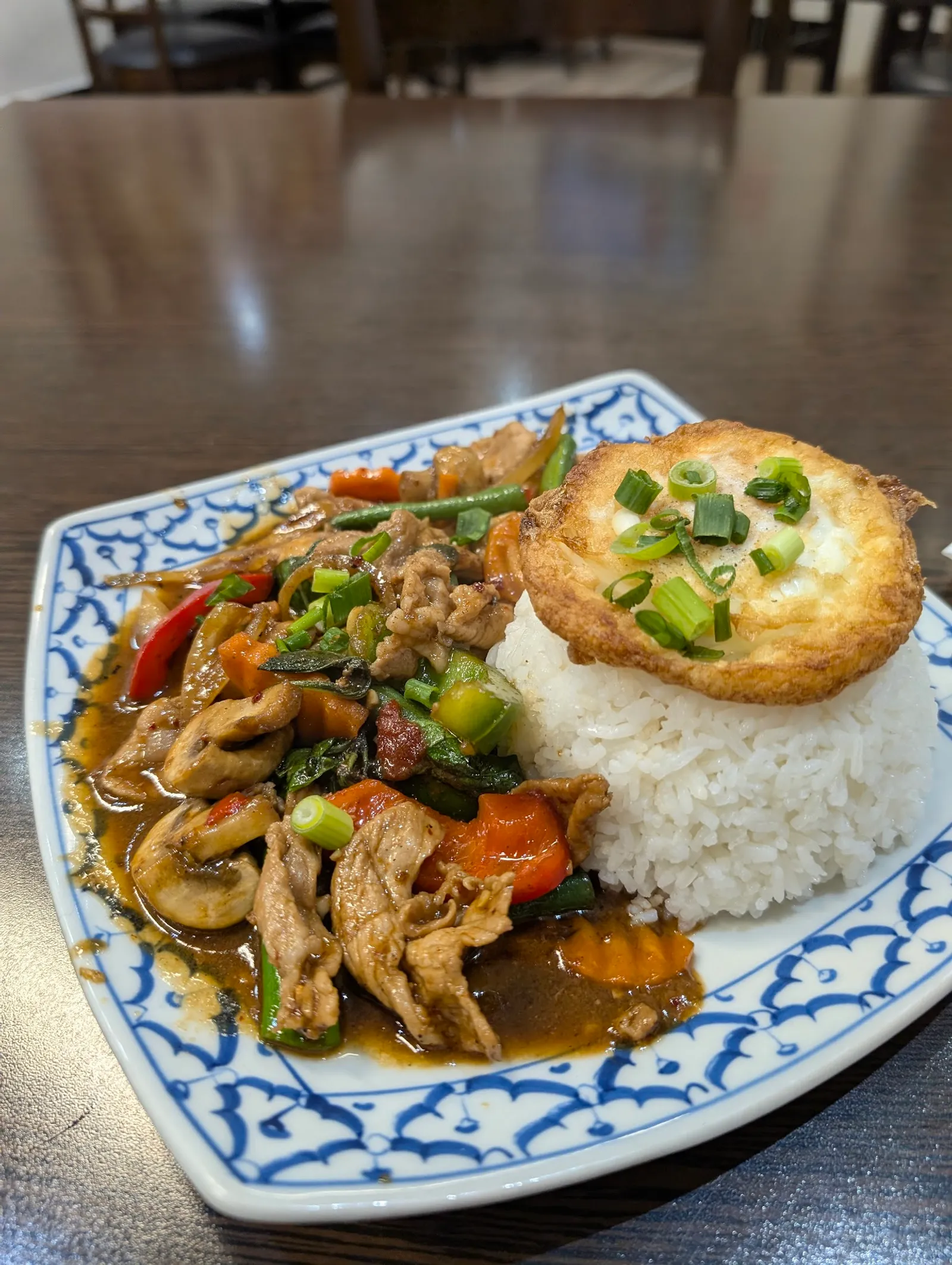 Thai basil stir-fry with fried egg and steamed rice on blue-white ceramic plate