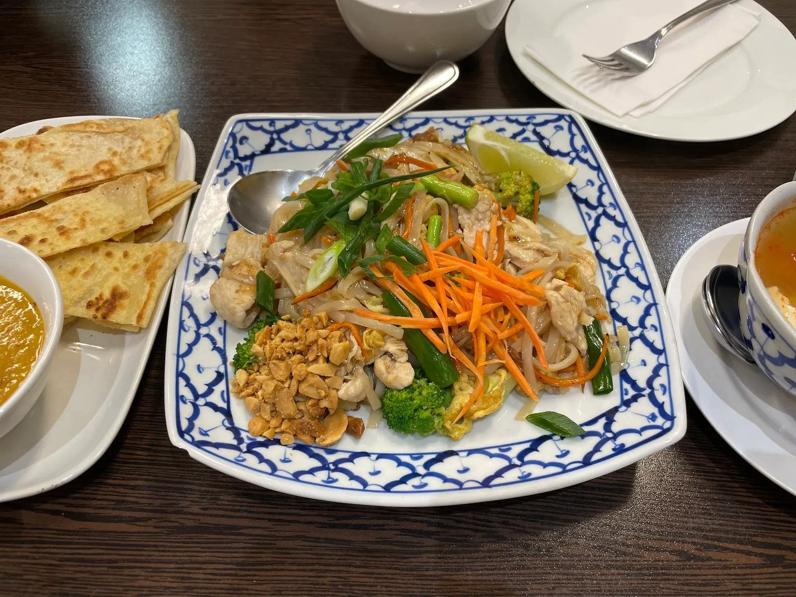 Thai chicken noodle stir-fry with roti and satay sauce on blue-white plates