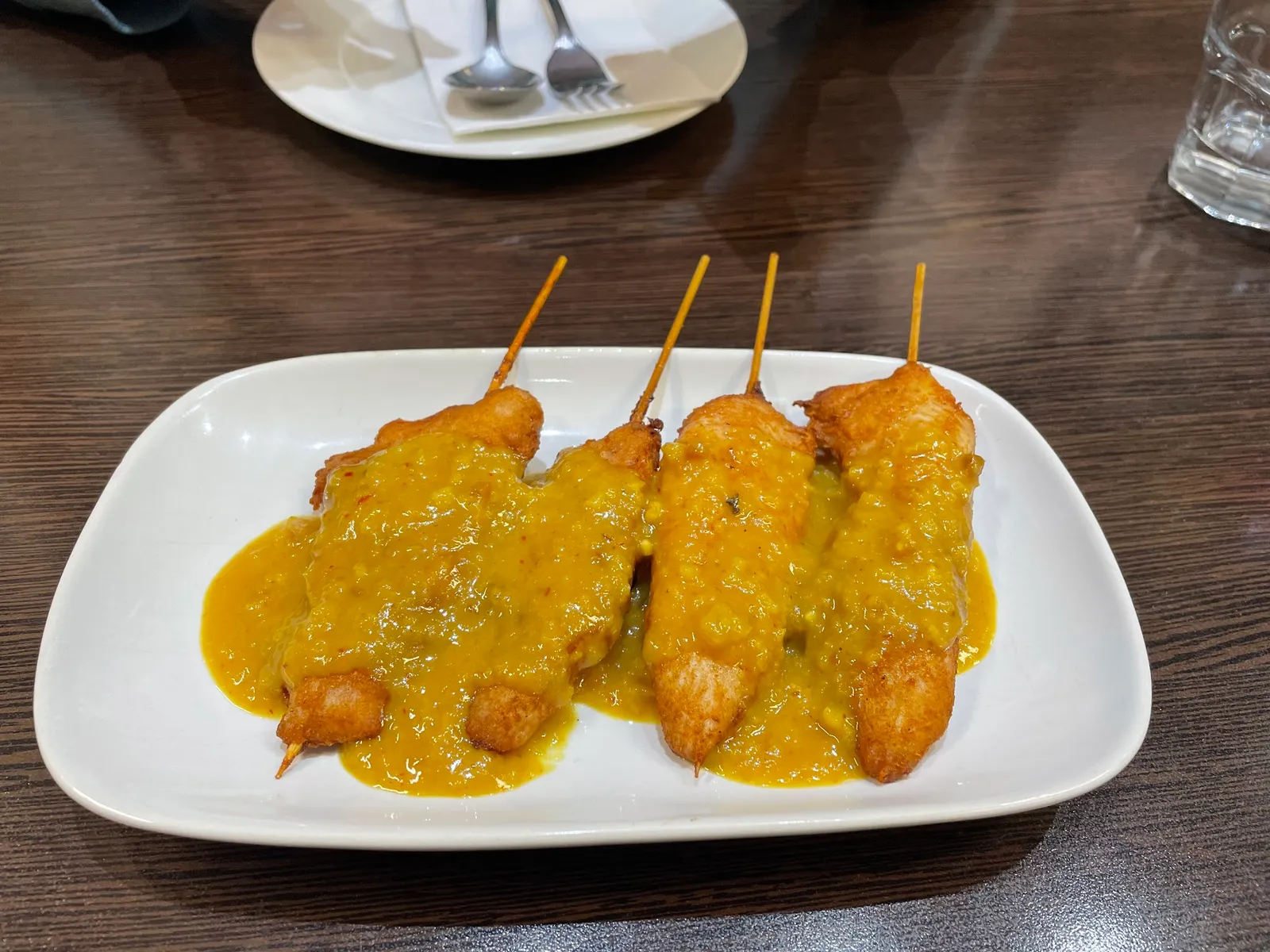 Four chicken satay skewers with peanut sauce on a white oval plate