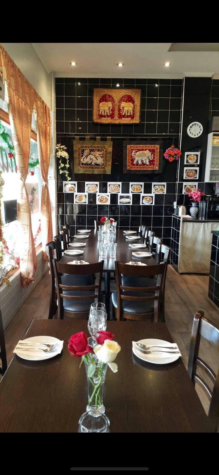 Baihmon Thai Restaurant dining room with set tables, rose centrepieces and Thai tapestries on black tiled walls